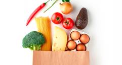 Paper grocery bag with vegetables, pasta, eggs and cheese top view isolated on white background