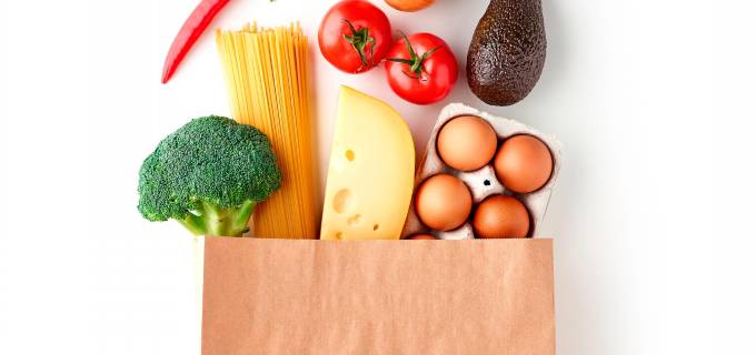 Paper grocery bag with vegetables, pasta, eggs and cheese top view isolated on white background