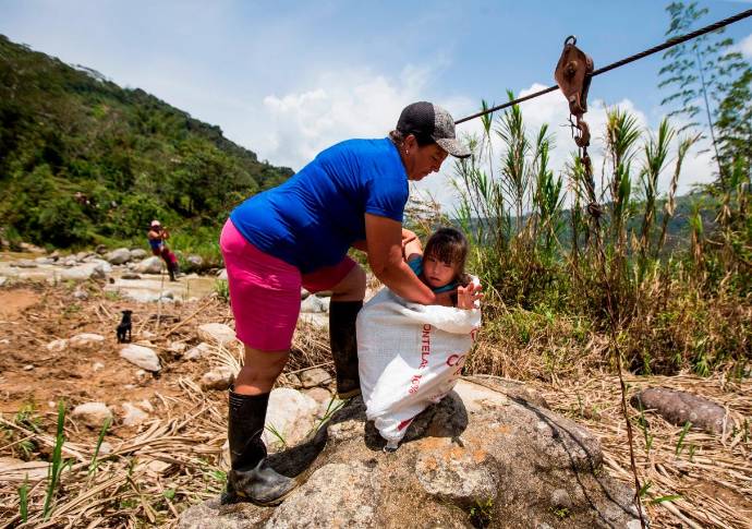 Una maniobra riesgosa, una niña es introducida en un costal, luego el costal se enclava en una polea, la niña queda encerrada y un adulto sentado en un lazo que le sirve de sillón carga la niña y se descuelga por una viga metálica para avanzar y pasar al otro lado del río. FOTO JULIO CÉSAR HERRERA