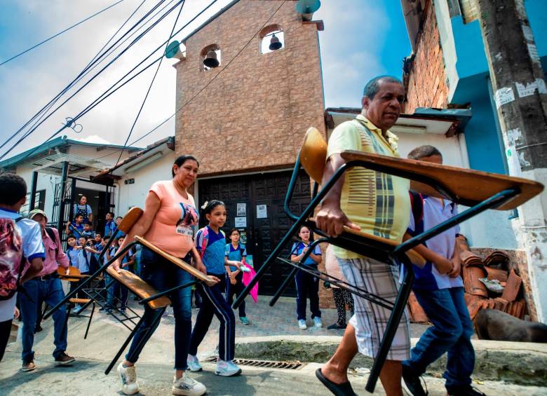 los niños con sus padres llevando los pupitres. 