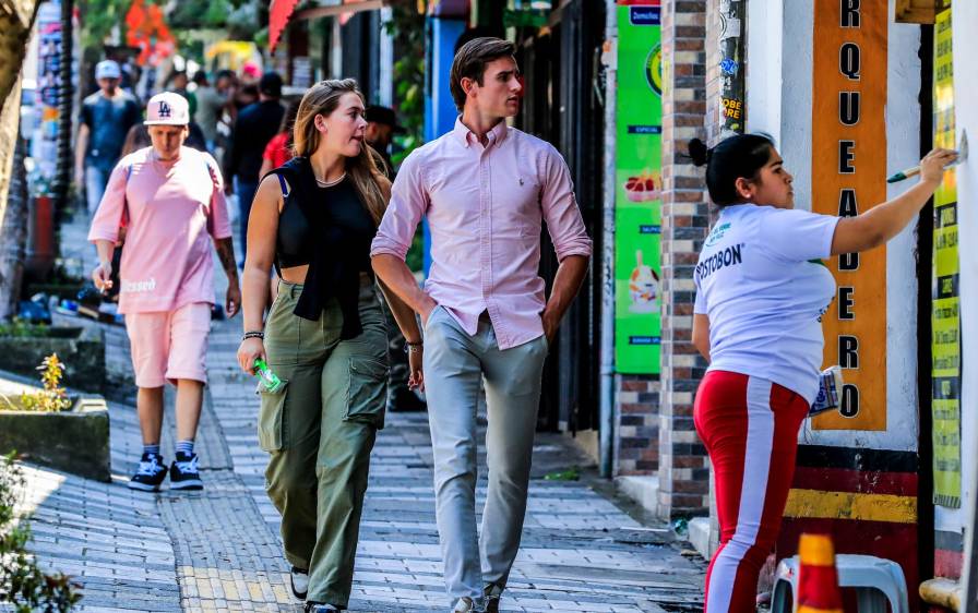 1) Extranjeros recorren la calle 10 en El Poblado. 2) Algunos, en la misma calle, compran varios productos. 3) Dos londinenses caminan por el segundo parque de Laureles. 4) Turistas recorren cerca de un acopio de taxis en el parque de El Poblado. FOTOS jaime pérez