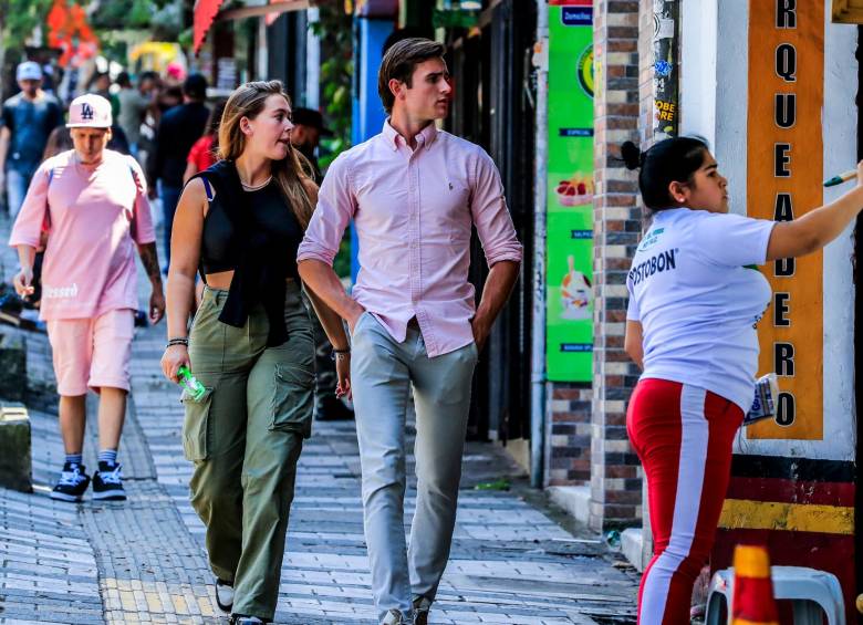 1) Extranjeros recorren la calle 10 en El Poblado. 2) Algunos, en la misma calle, compran varios productos. 3) Dos londinenses caminan por el segundo parque de Laureles. 4) Turistas recorren cerca de un acopio de taxis en el parque de El Poblado. FOTOS jaime pérez