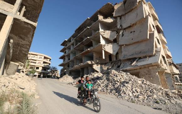 Syrian men ride a motorcycle past heavily-damaged buildings in the rebel-held town of Maaret al-Numan, in the north of Idlib province on September 27, 2018. OMAR HAJ KADOUR / AFP