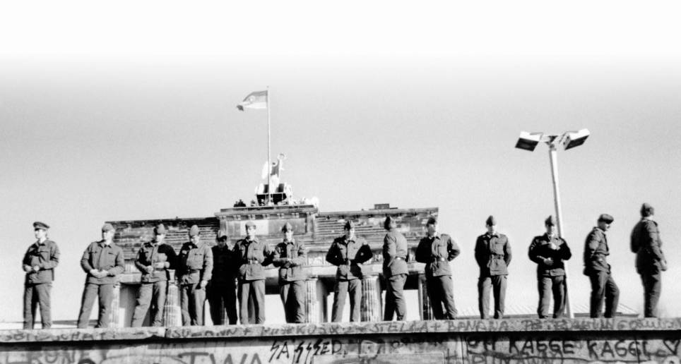 Soldados fronterizos del Este sobre una parte del Muro de Berlín con la Puerta de Brandenburgo de fondo. FOTO AFP